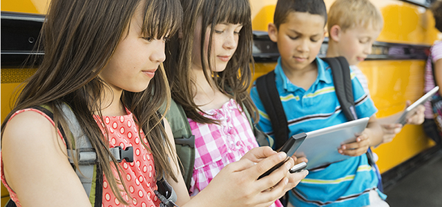 Kids on mobile devices near a school bus