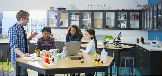 Group of kids collaborating at a computer with a teacher